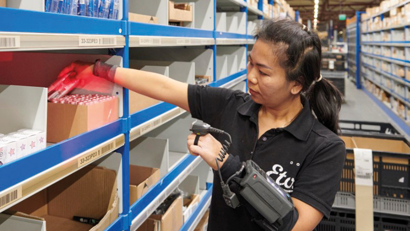 A woman with a scanner on her forearm is stocking the shelves at Etos.